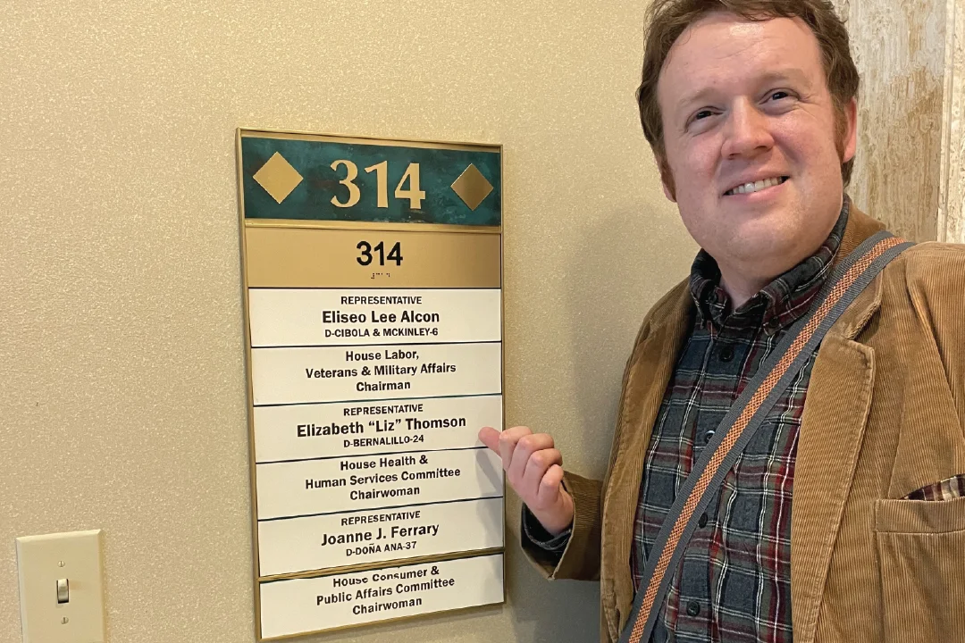 Dr. Anderson smiling next to wayfinding signage for New Mexico representative