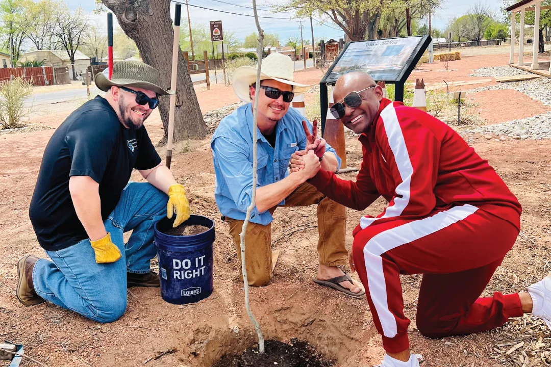 three men gathered smiling while planting a tree