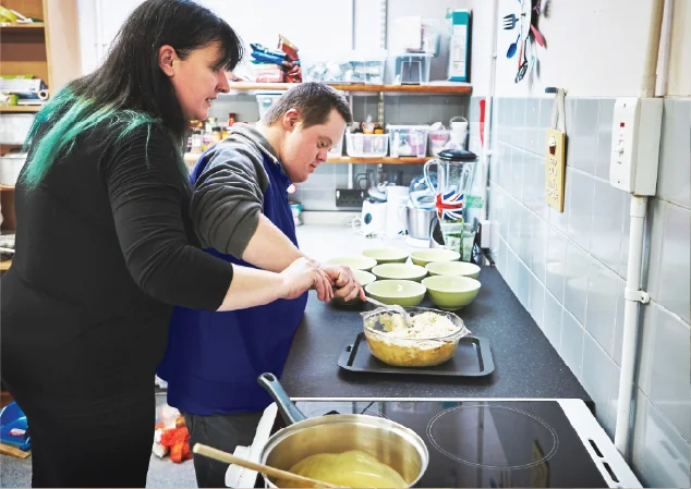 Volunteer helping young adult male with special needs learning to cook