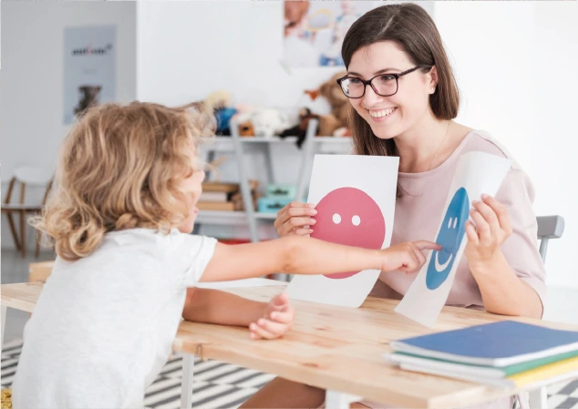 teacher holding two cards to student pointing at one of the cards